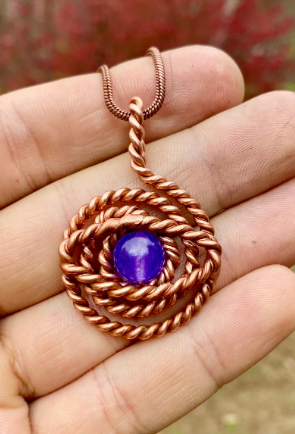 Copper necklace with a purple gemstone held in a hand against a blurred natural background