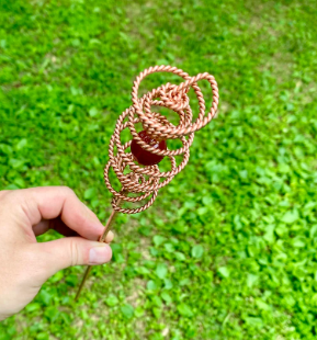 Hand holding a copper-colored decorative object against a green grass background