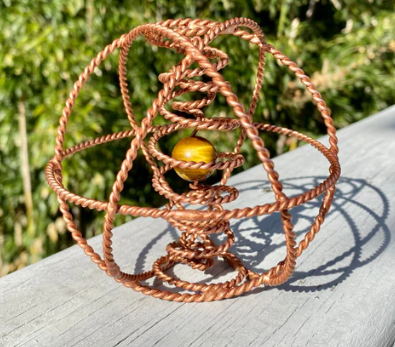 Copper wire sculpture on a wooden surface with greenery in the background
