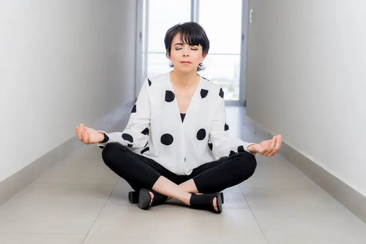 Woman meditating indoors in lotus position, promoting wellness and relaxation