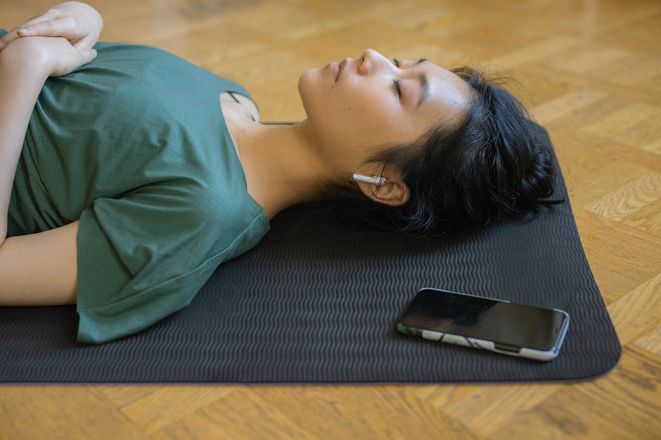 Woman relaxing on a black wellness mat with phone nearby, promoting energy and wellness technology.
