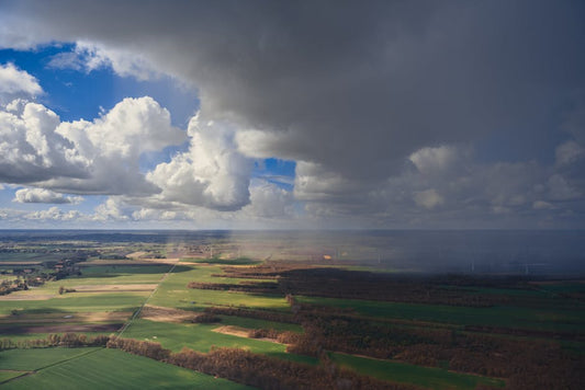 Aerial view of green farmland under dramatic clouds and sunlight, natural landscape scenery.