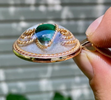 Gold pendant with green gemstone held by a hand against a blurred background