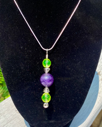Necklace with green and purple beads on a black stand