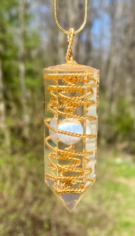 Crystal pendant with gold spiral design and a white sphere, hanging against a blurred natural background.
