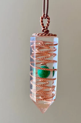 Crystal pendant with copper spiral and green bead on a plain background