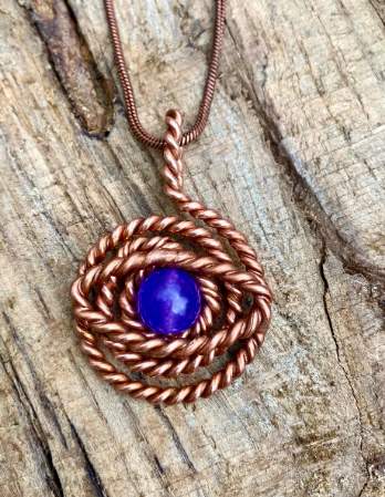 Copper necklace with a purple gemstone on a wooden surface