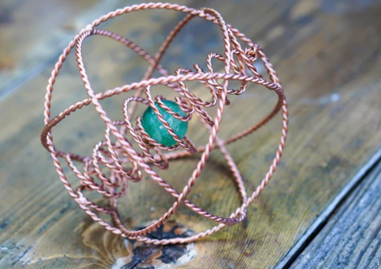 Copper wire-wrapped ring with a green gemstone on a wooden surface