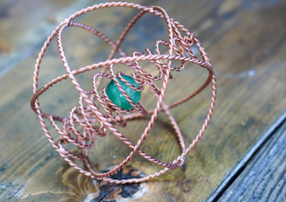 Copper wire-wrapped ring with a green gemstone on a wooden surface