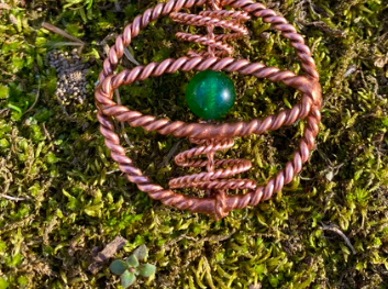 Copper wire ring with a green stone on a mossy background