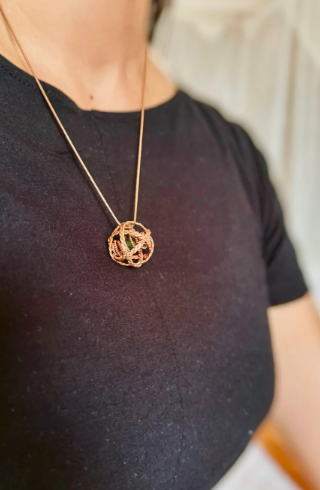 Person wearing a gold necklace with a spherical pendant against a neutral background