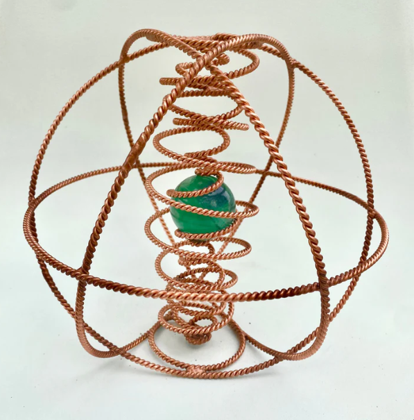 Copper coil structure with a green sphere at its center on a white background