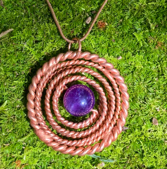 Copper spiral necklace with a purple gemstone on a green moss background