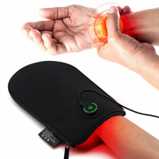 A black infrared LED light therapy mitten being worn on a person's hand, with red light emitting from the mitten.
