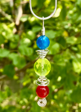 Necklace with blue, green, and red beads against a blurred green leafy background