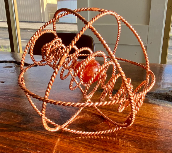 Copper wire sculpture on a wooden surface with a blurred background