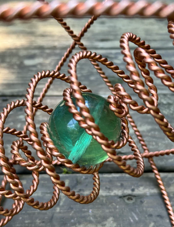 Green fluorite crystal sphere encased in twisted copper wire on a wooden surface
